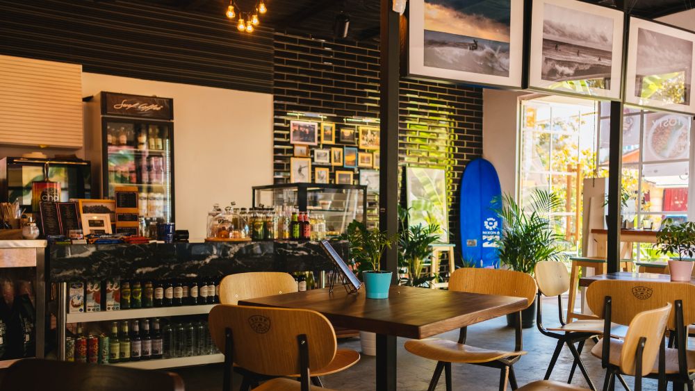 Empty cafe with tables, chairs, hanging artwork, and stocked food items