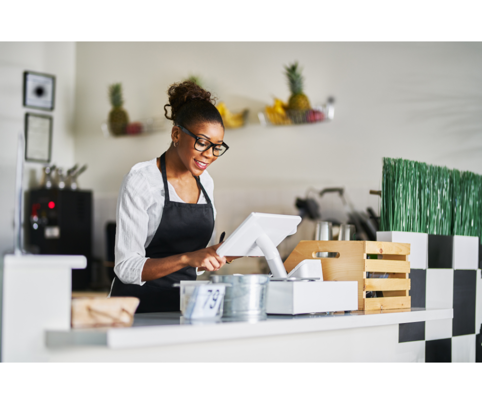 Woman working at a point of sales machine in a cafe setting.